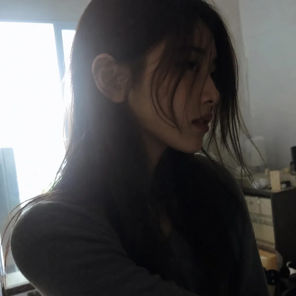 Colour phone snapshot of a young woman turned away from the camera, half her face in deep shadow with hair falling across it, slightly out of focus